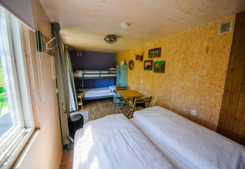 Pequeña casa luminosa con litera, cama doble, mesa comedor y grandes ventanas con vistas al exterior verde.