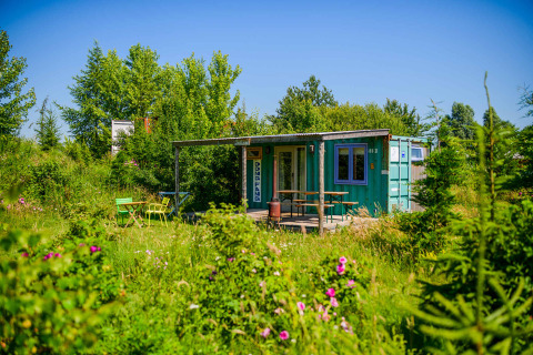 Una tiny house de contenedor marítimo en Netl Camping Kallumaan, Países Bajos, rodeada de vegetación y flores.