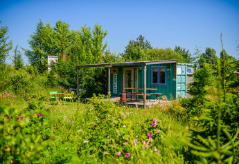 Una tiny house de contenedor marítimo en Netl Camping Kallumaan, Países Bajos, rodeada de vegetación y flores.