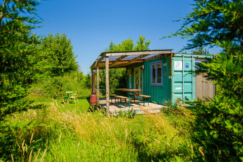 Casa diminuta de contenedor marítimo verde con porche en Netl Camping Kallumaan, Países Bajos, rodeada de naturaleza.