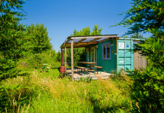 Casa diminuta de contenedor marítimo verde con porche en Netl Camping Kallumaan, Países Bajos, rodeada de naturaleza.