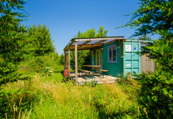 Grøn shipping container tiny house med terrasse på Netl Camping Kallumaan, omgivet af grønt og natur.