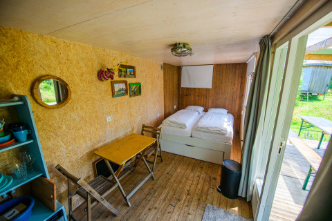 Intérieur lumineux d’une tiny house avec deux lits simples, table, chaises et accès à l’extérieur.