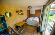 A bright and cozy tiny house interior with twin beds, small dining table, chairs, and access outdoors.