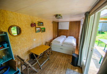 Interior de casa pequeña acogedora, con dos camas individuales, mesa plegable, sillas y salida al jardín.