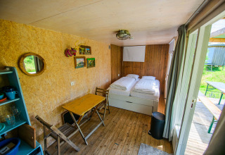 Gezellige tiny house met twee enkele bedden, kleine tafel, stoelen en schuifdeur naar de buitenruimte.