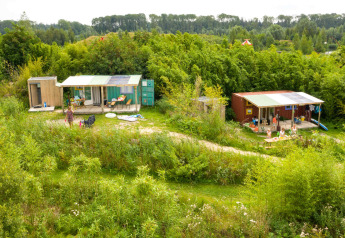 Casa pequeña de contenedor marítimo con fontanería, rodeada de naturaleza y personas en el exterior.