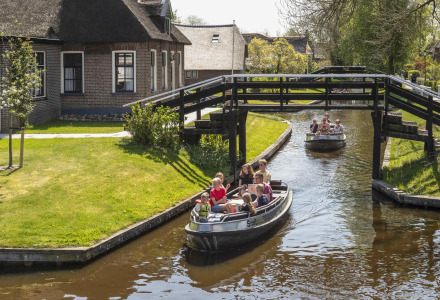 Personas navegando en barcas por un canal rodeado de casas tradicionales y puentes de madera en Holanda.