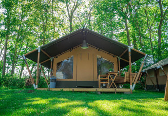 Das Lodge Compact auf Camping de Tolbrug in den Niederlanden, umgeben von grüner Wiese und Bäumen.