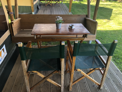 Wooden outdoor table and two green chairs at Lodge Compact, Camping de Tolbrug, Netherlands, on a deck.