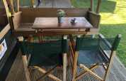 Wooden outdoor table and two green chairs at Lodge Compact, Camping de Tolbrug, Netherlands, on a deck.