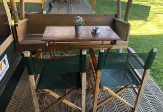 Mesa de madera y dos sillas verdes en Lodge Compact, Camping de Tolbrug, Países Bajos, sobre tarima exterior.