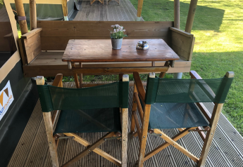Wooden outdoor table and two green chairs at Lodge Compact, Camping de Tolbrug, Netherlands, on a deck.