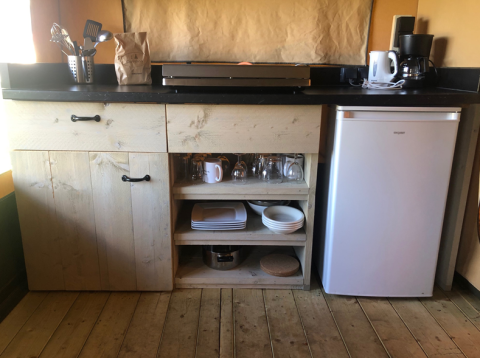 Kleine Küchenzeile der Lodge Compact auf Camping de Tolbrug, Niederlande, mit Kühlschrank und Geschirr.