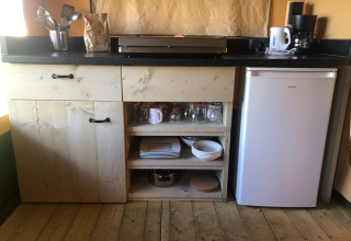 Kleine Küchenzeile der Lodge Compact auf Camping de Tolbrug, Niederlande, mit Kühlschrank und Geschirr.