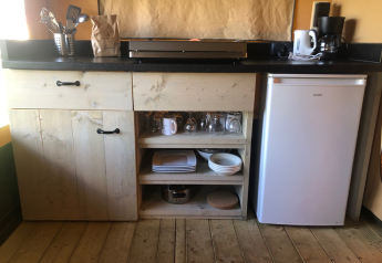 Kleine Küchenzeile der Lodge Compact auf Camping de Tolbrug, Niederlande, mit Kühlschrank und Geschirr.