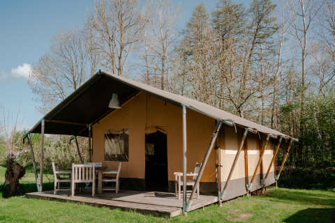Safaritent met terras en tuinmeubilair bij Camping De Rammelbeek in Nederland, zonnig en groen uitzicht.