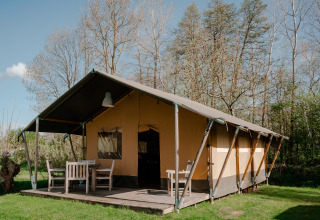 Safari tent with porch and outdoor furniture at Camping De Rammelbeek in the Netherlands on a sunny day.