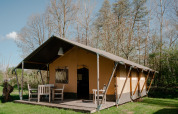 Safaritent met terras en tuinmeubilair bij Camping De Rammelbeek in Nederland, zonnig en groen uitzicht.