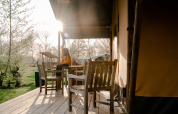 En person sidder på en terrasse foran et safaritelt med træmøbler og morgensol på Camping De Rammelbeek.