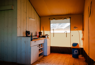 Interior de tienda safari con cocina pequeña y papelera en Camping De Rammelbeek, Países Bajos.
