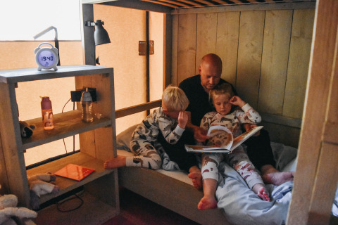 Famiglia che legge una fiaba nella tenda safari con servizi al Camping De Rammelbeek, Paesi Bassi.