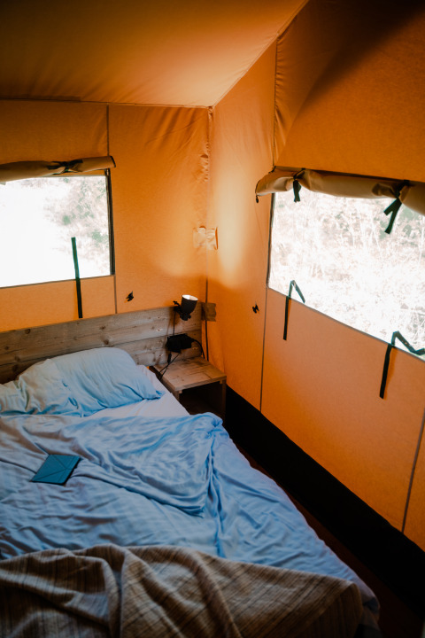 Interieur van een safaritent met bed en lamp bij Camping De Rammelbeek in Nederland, gezellige sfeer.