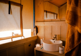 Interior de tienda safari con baño privado en Camping De Rammelbeek, Países Bajos, luz cálida entrando.