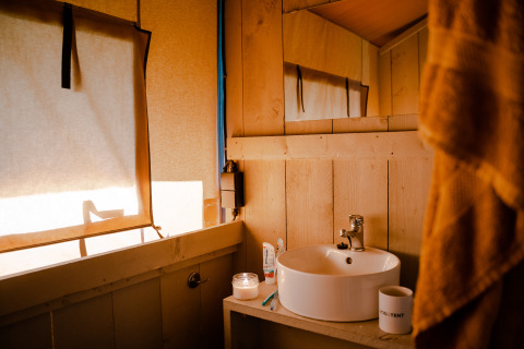 Binnenkant van een safaritent met privé sanitair op Camping De Rammelbeek in Nederland, zonlicht schijnt in.