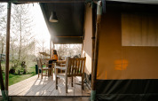 Kvinde sidder på terrasse foran safaritelt med eget bad på Camping De Rammelbeek, Holland, i solnedgang.