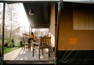 Mujer sentada en la terraza de una tienda safari con baño en Camping De Rammelbeek, Países Bajos, al atardecer.