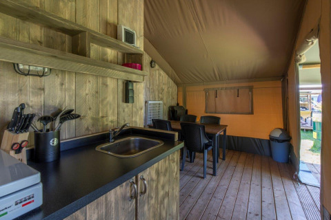 Interior de tienda safari con cocina, mesa comedor y suelo de madera en Camping De Rammelbeek, Países Bajos.