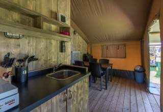 Interior de tienda safari con cocina, mesa comedor y suelo de madera en Camping De Rammelbeek, Países Bajos.