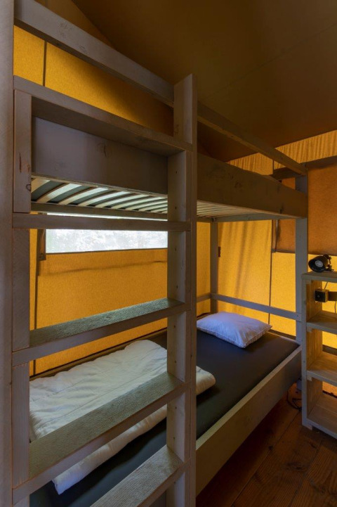 Interieur van een safaritent bij Camping De Rammelbeek met stapelbed, houten planken en geel doek.