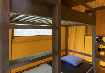 Interno di una tenda safari al Camping De Rammelbeek con letto a castello, scaffali in legno e telo giallo.