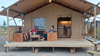 Persone che si rilassano sul portico di una tenda safari con braciere e servizi igienici moderni.