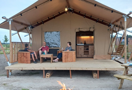 Mensen genieten op het terras van een safaritent met vuurkorf en comfortabele sanitaire voorzieningen.