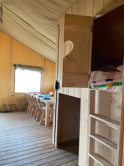 Interieur van een safaritent bij Minicamping Hofstede Zonnevliet met houten meubels en kleurrig beddengoed.