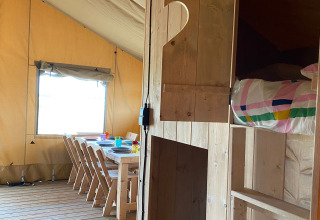Interior de una tienda safari en Minicamping Hofstede Zonnevliet con muebles de madera y ropa de cama colorida.