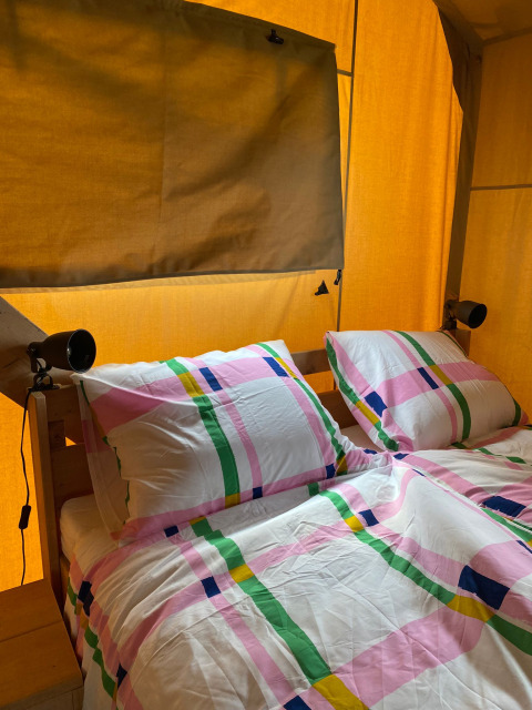 Vista interior de una tienda safari con ropa de cama colorida e instalaciones sanitarias en Minicamping Hofstede Zonnevliet.