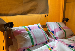 Vista interior de una tienda safari con ropa de cama colorida e instalaciones sanitarias en Minicamping Hofstede Zonnevliet.