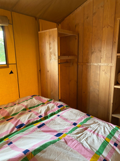 Interior de una tienda safari con paredes de madera, estantes y ropa de cama colorida en Minicamping Hofstede Zonnevliet.