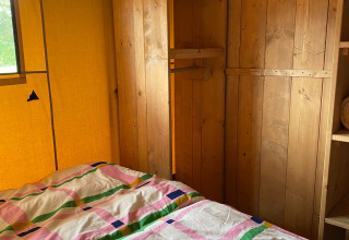 Interior de una tienda safari con paredes de madera, estantes y ropa de cama colorida en Minicamping Hofstede Zonnevliet.