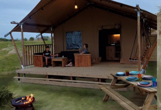 Tienda safari con terraza y fogata en Minicamping Hofstede Zonnevliet, Países Bajos, personas relajándose.