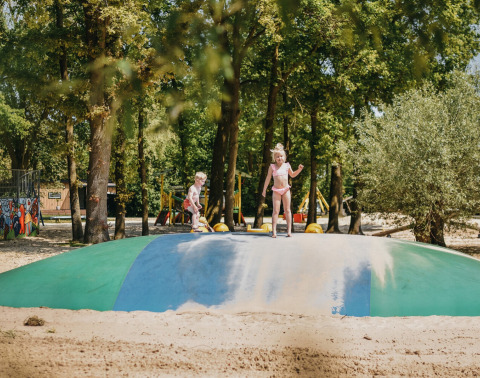 Kinder spielen auf einem großen Hüpfkissen im Sand im Ferienpark Camping De Rammelbeek, Overijssel.