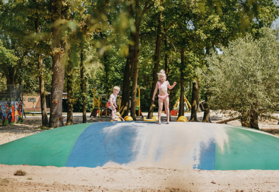 Kinder spielen auf einem großen Hüpfkissen im Sand im Ferienpark Camping De Rammelbeek, Overijssel.