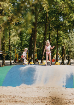 Kinder spielen auf einem großen Hüpfkissen im Sand im Ferienpark Camping De Rammelbeek, Overijssel.