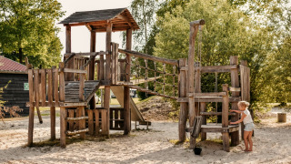 Houten speeltuin bij Camping De Rammelbeek in Overijssel, Nederland, met spelend kind in het zand.