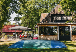 Außenszene beim Camping De Rammelbeek in Overijssel, Niederlande, mit Terrasse, Haus und schattigen Bäumen.