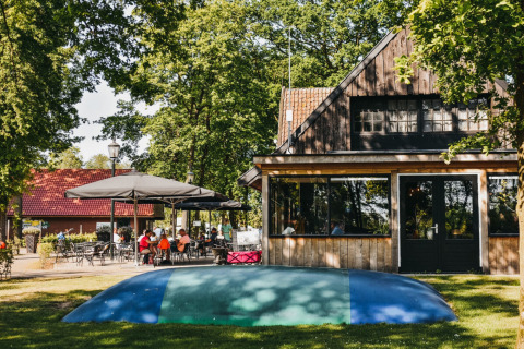 Udendørs scene på Camping De Rammelbeek i Overijssel, Holland, med hytter, parasoller og gæster ved bordene.